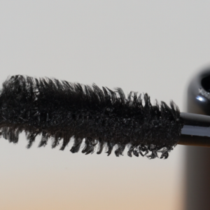 A close-up of a mascara wand with black globs on the bristles.