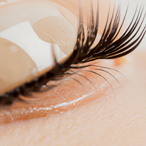 A close-up of a pair of eyelashes with a drop of serum on them.