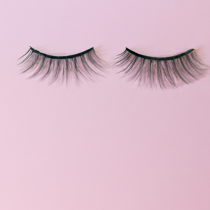 A close-up of a pair of false eyelashes with a light pink background.