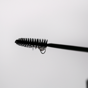 A close-up of a mascara brush, dripping with water droplets.